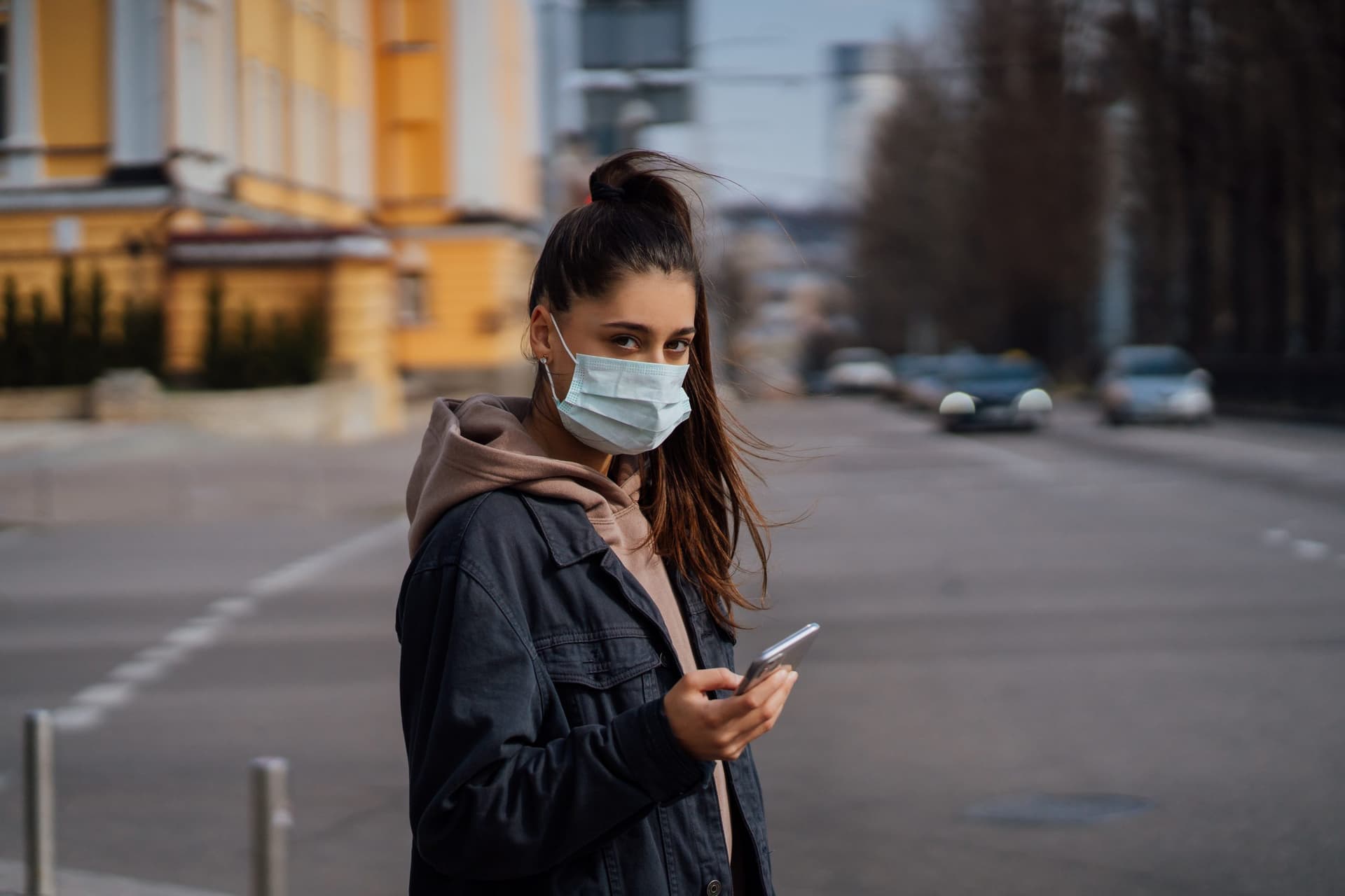 Girl in protective mask using smartphone outdoors. COVID 19. World coronavirus pandemic.